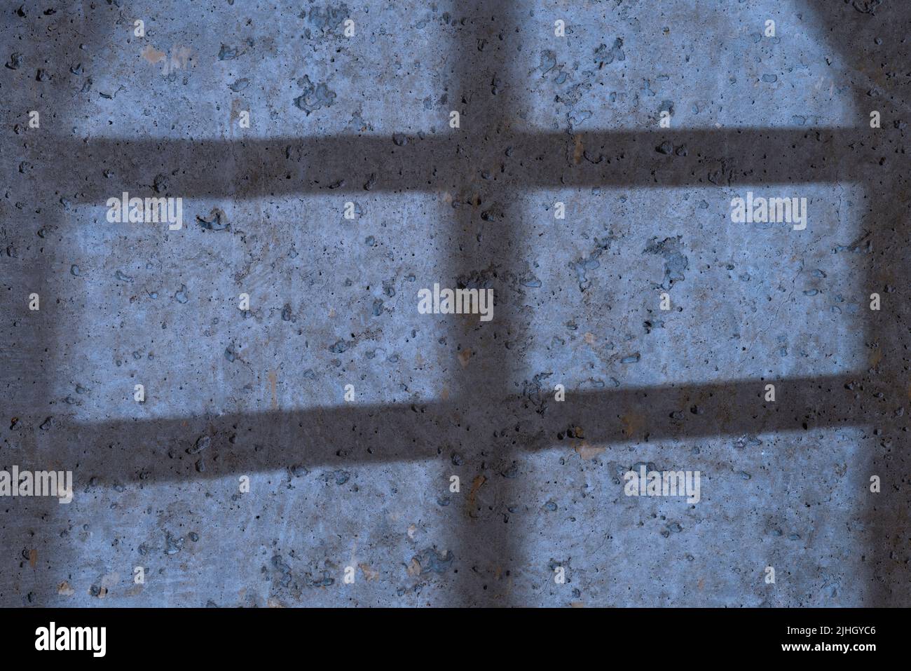 Shadow from a barred window on a rough concrete wall. Moonlight lighting. Prison, jail or basement theme Stock Photo