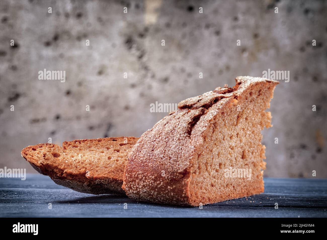 Two pieces of bread on a wooden table against a rough wall. Simple food theme still life Stock Photo