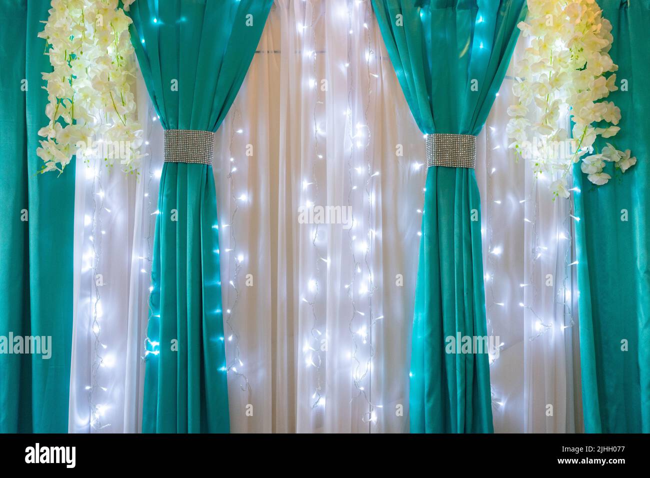 Decoration of the banquet hall with white and turquoise fabric illuminated with garlands. Stock Photo