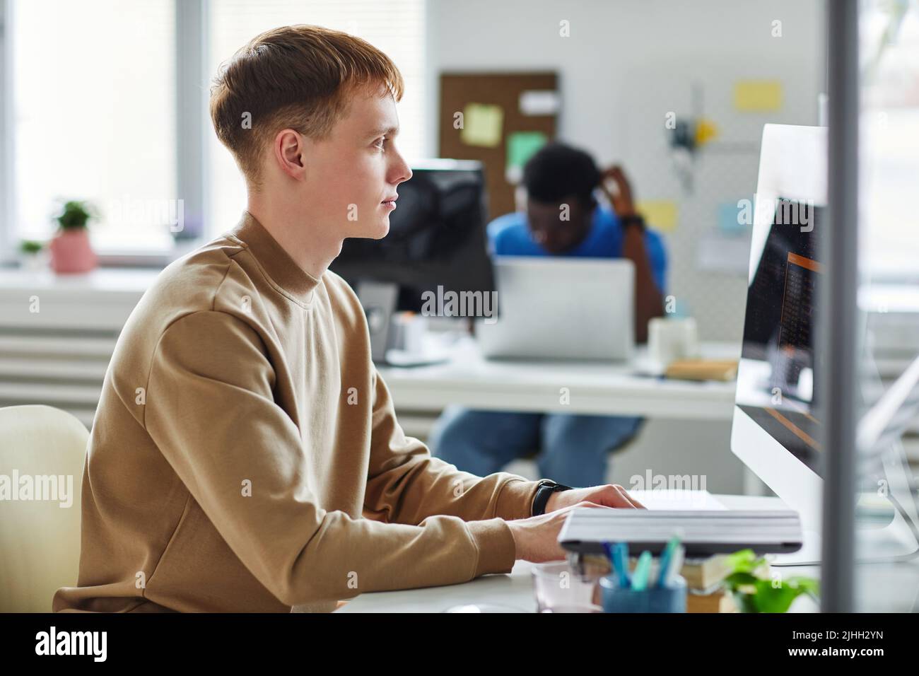 Profile view of young programmer working on computer in IT office typing data coding in software at his workplace Stock Photo