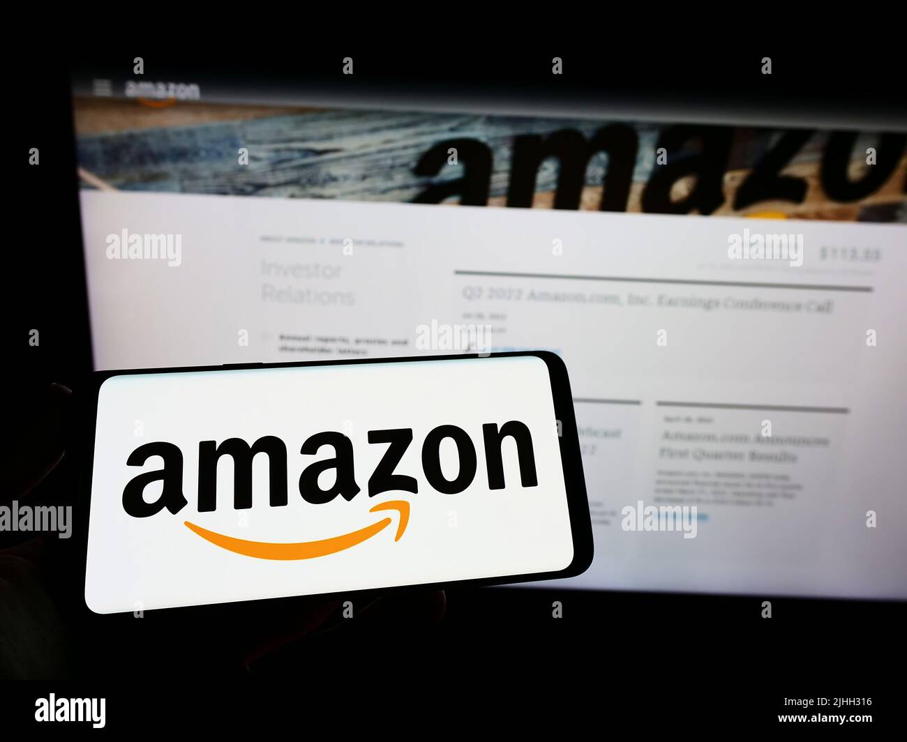 Person holding mobile phone with logo of American technology company Amazon.com Inc. on screen in front of web page. Focus on phone display. Stock Photo