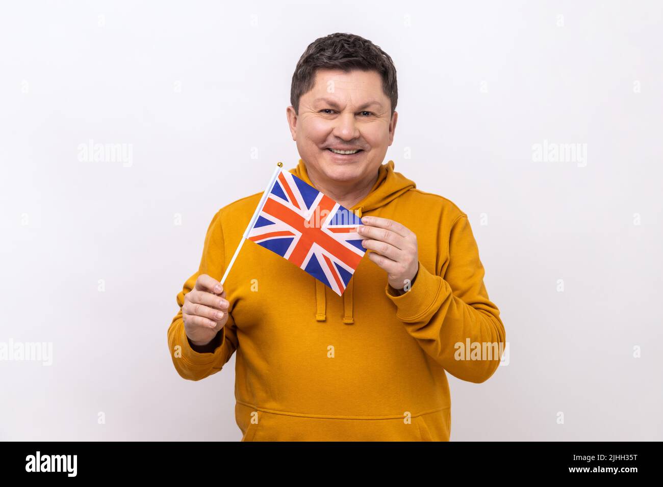 Portrait of smiling delighted handsome middle aged man holding flag of United Kingdom of Great Britain, wearing urban style hoodie. Indoor studio shot isolated on white background. Stock Photo