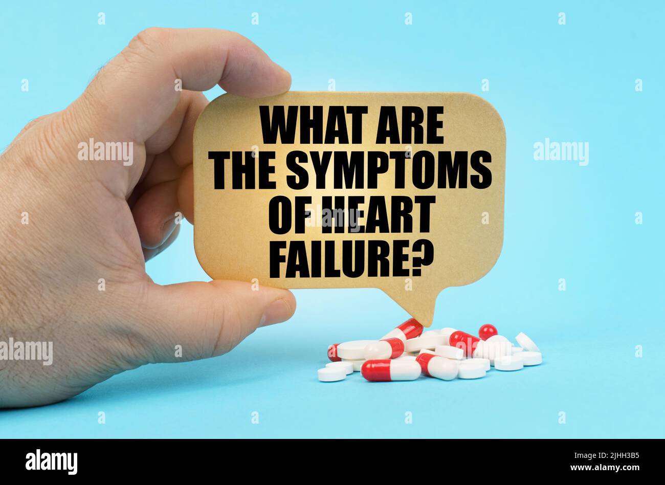 Medical concept. On a blue surface are pills in a persons hand, a sign with  the inscription - What are the symptoms of heart failure Stock Photo - Alamy
