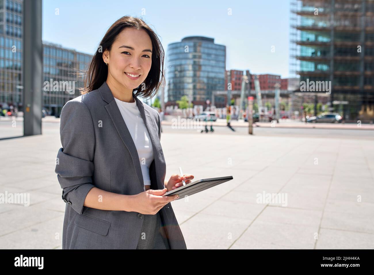 Young happy Asian business woman standing on city street holding digital tablet. Stock Photo