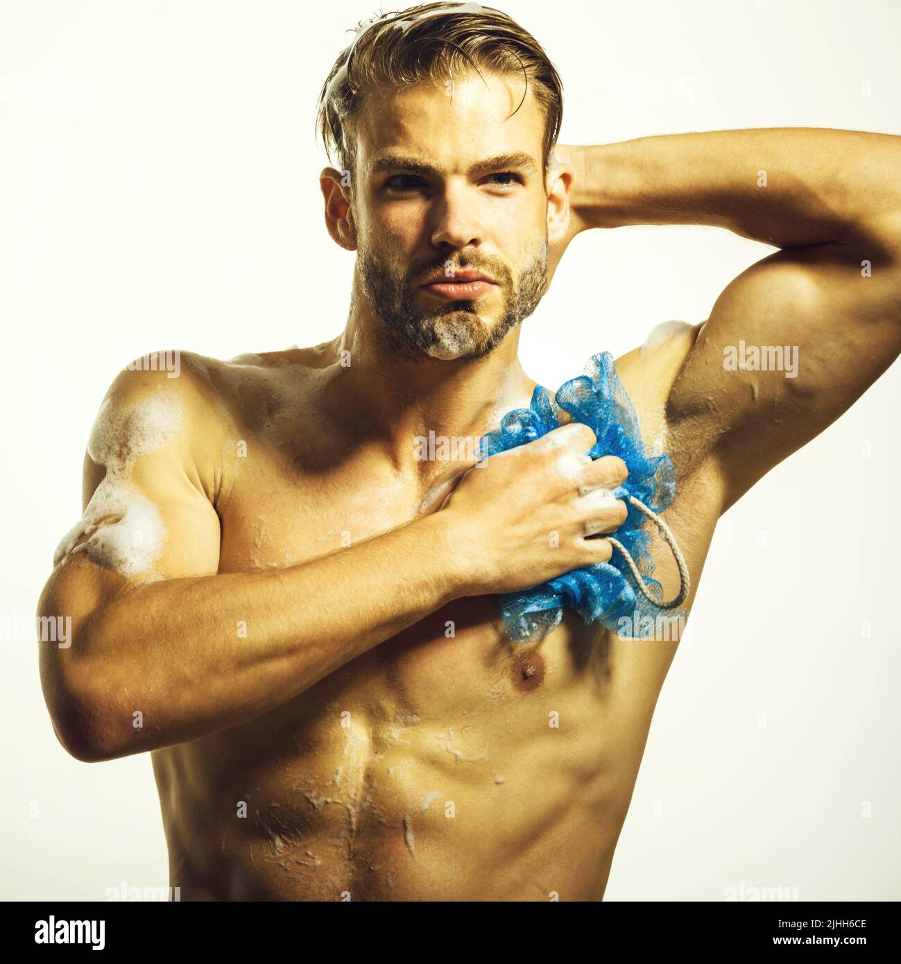 Handsome muscular guy at shower. Mens cosmetics for body care. Man washing with sponge in bathroom. Stock Photo