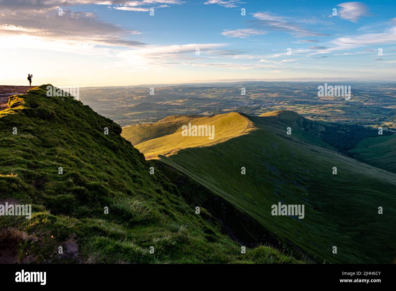 View of a man taking photos ontop of a mountain taking in the news at pen y fan brecon beacons south wales uk Stock Photo