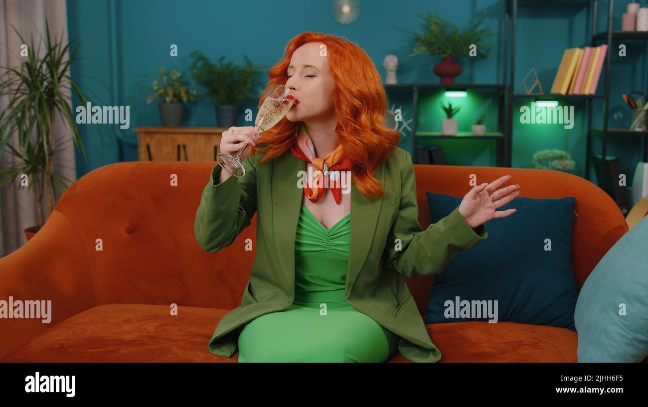 Joyful redhead woman hold glass of champagne cheering and drinking