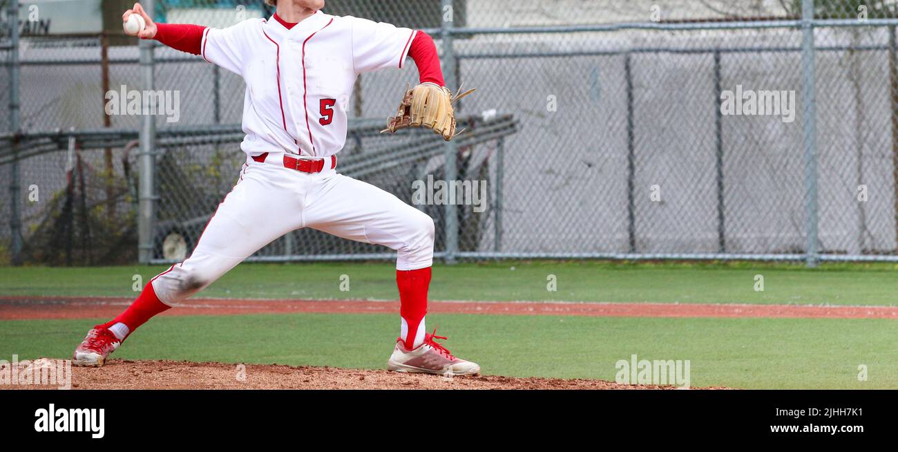 Side view of a high school pitcher pitching from the pitching mound during a game. Stock Photo