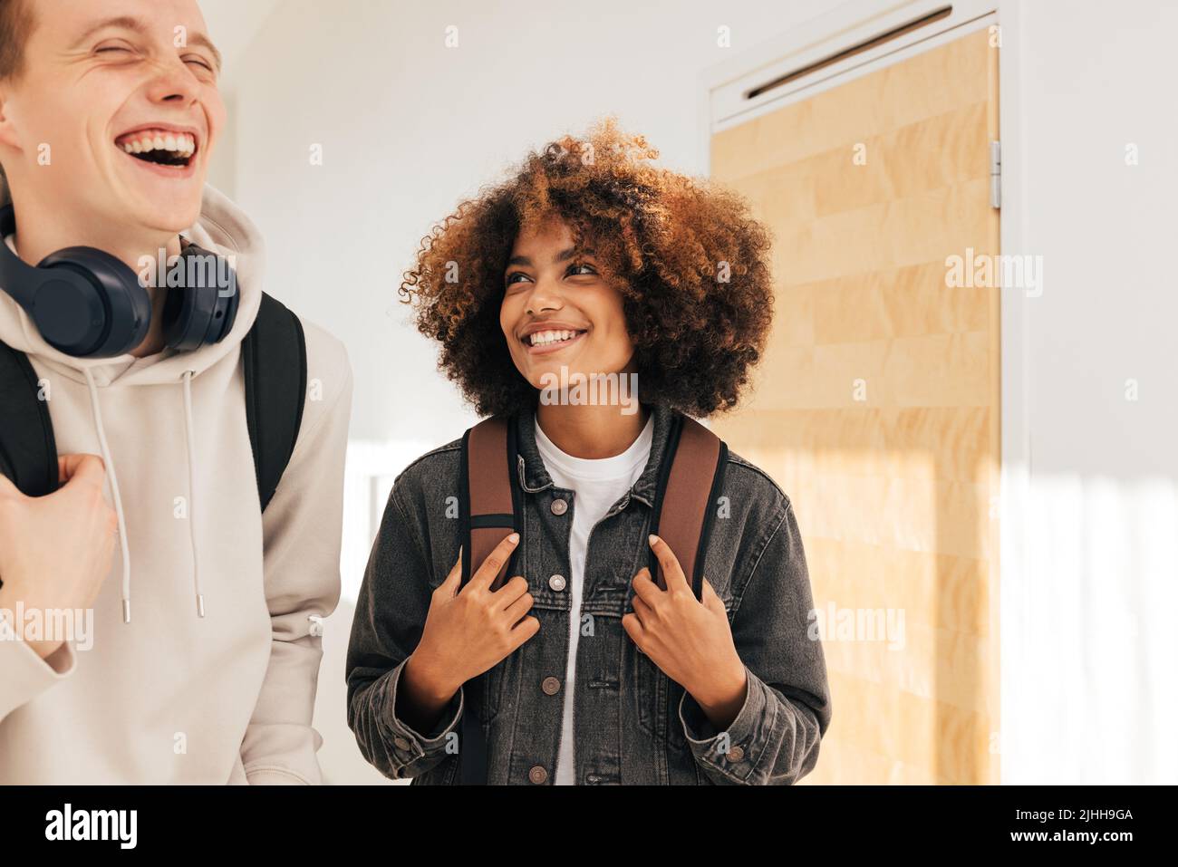 Two laughing teenagers in college. Smiling girl looking at her classmate in corridor. Stock Photo