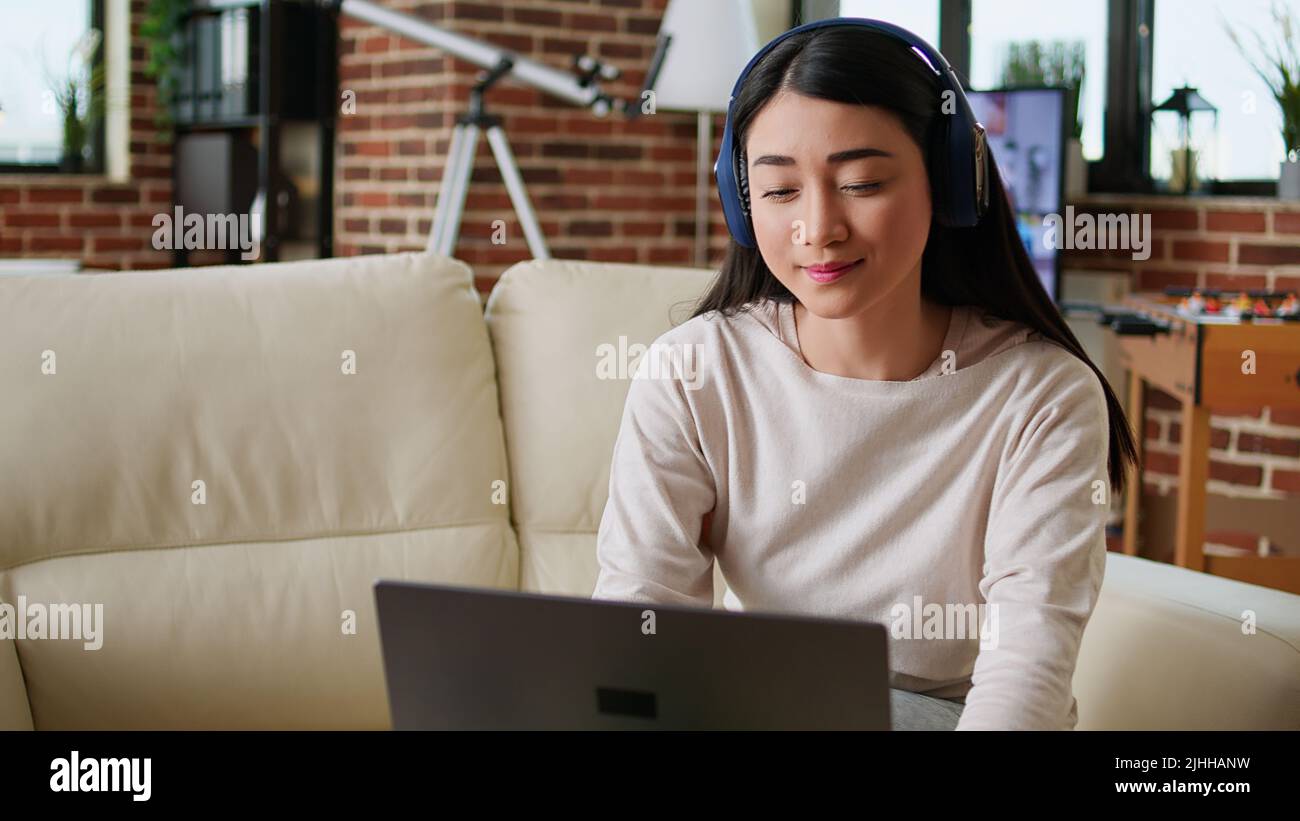 Cheerful woman wearing wireless headphones while working remotely at ...