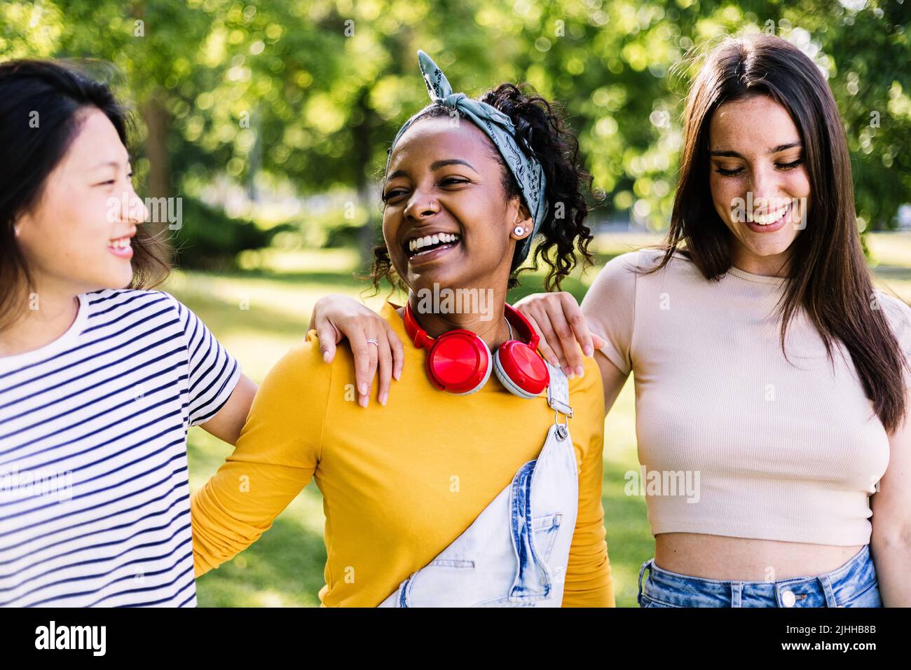 Three multiracial best woman friends laughing together in public park Stock Photo