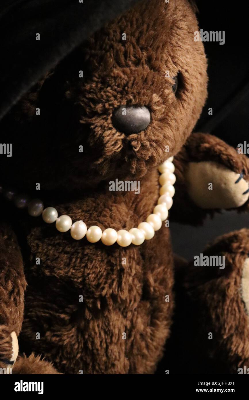 A brown teddy bear from the 1980s dressed in an oversized woman's hat and pearl necklace. Stock Photo