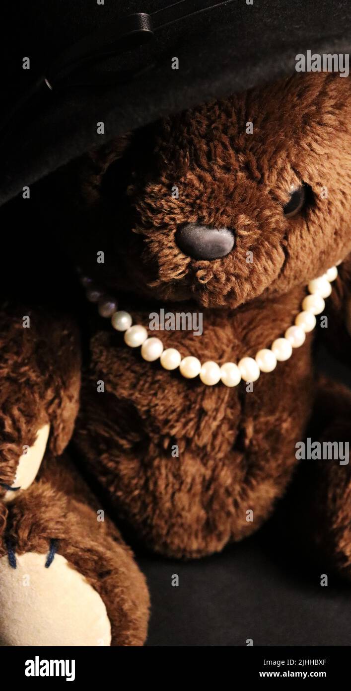 A brown teddy bear from the 1980s dressed in an oversized woman's hat and pearl necklace. Stock Photo