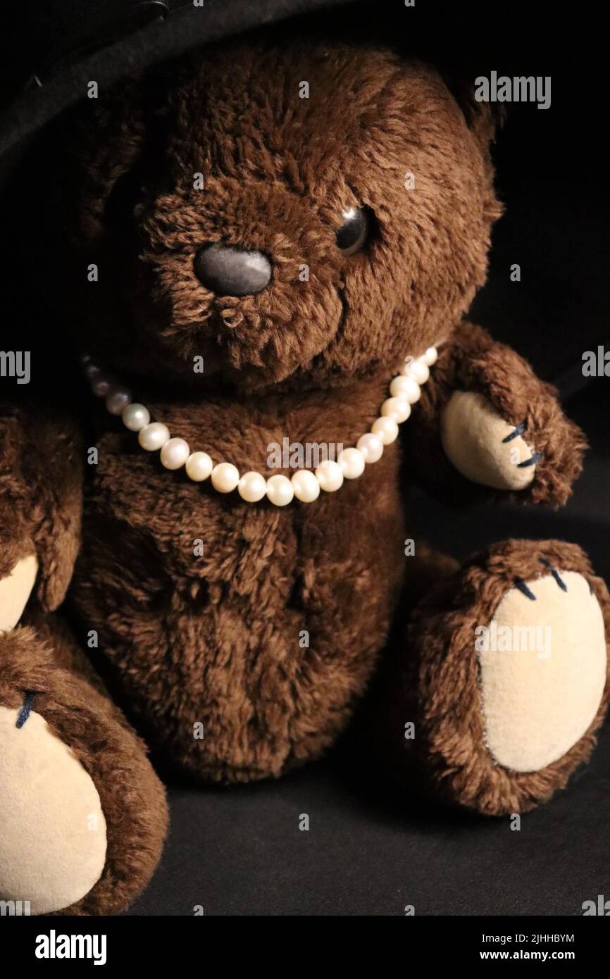 A brown teddy bear from the 1980s dressed in an oversized woman's hat and pearl necklace. Stock Photo