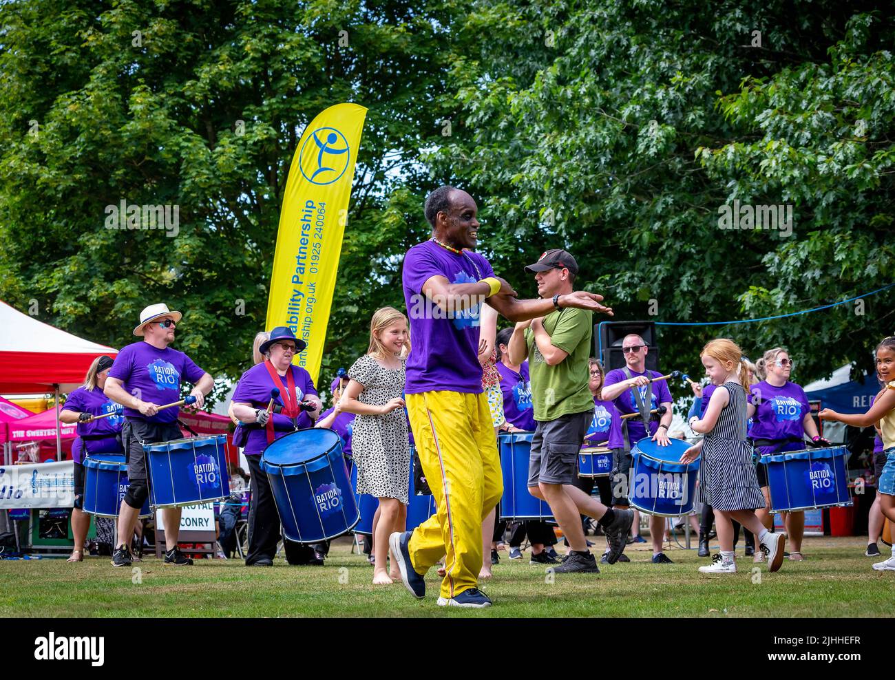 Colourful black man leads the children in dance with Batida Rio Samba Band at Disability Awareness Day 2022 Stock Photo