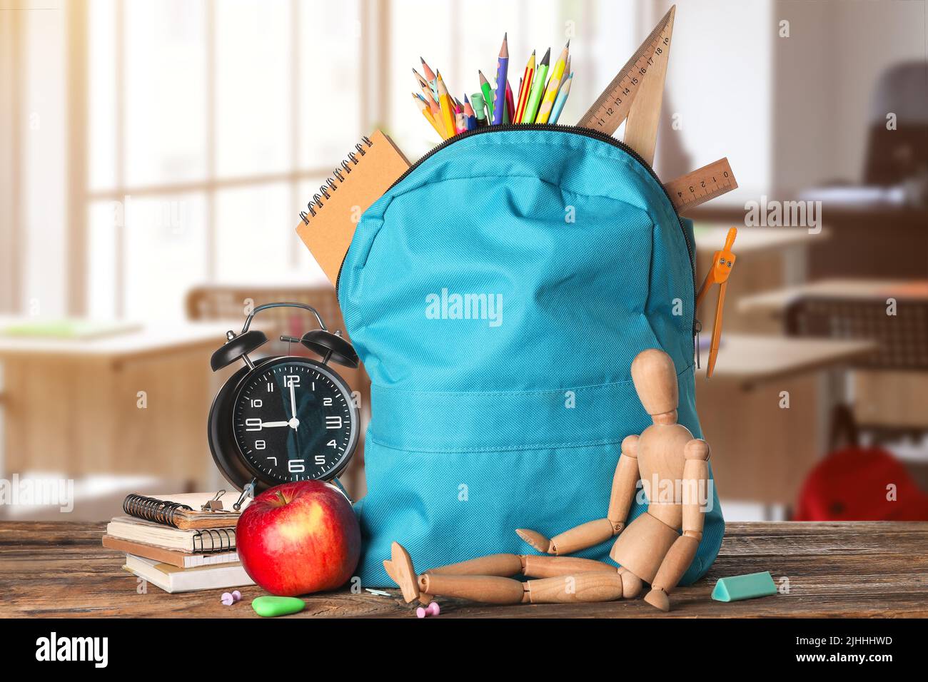 School backpack with stationery, wooden human figurine, clock and apple