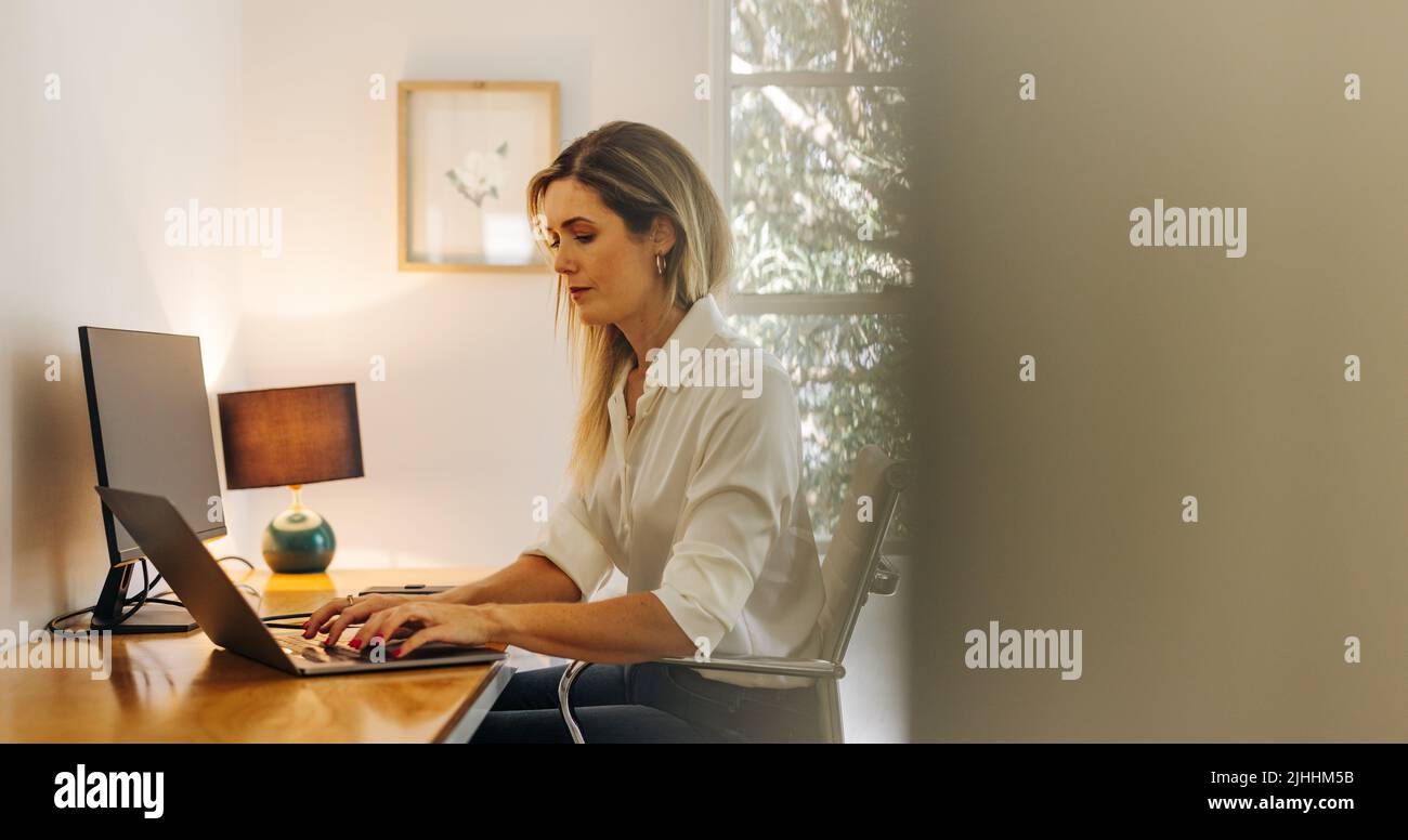 Young businesswoman typing on a laptop while sitting in her home office ...