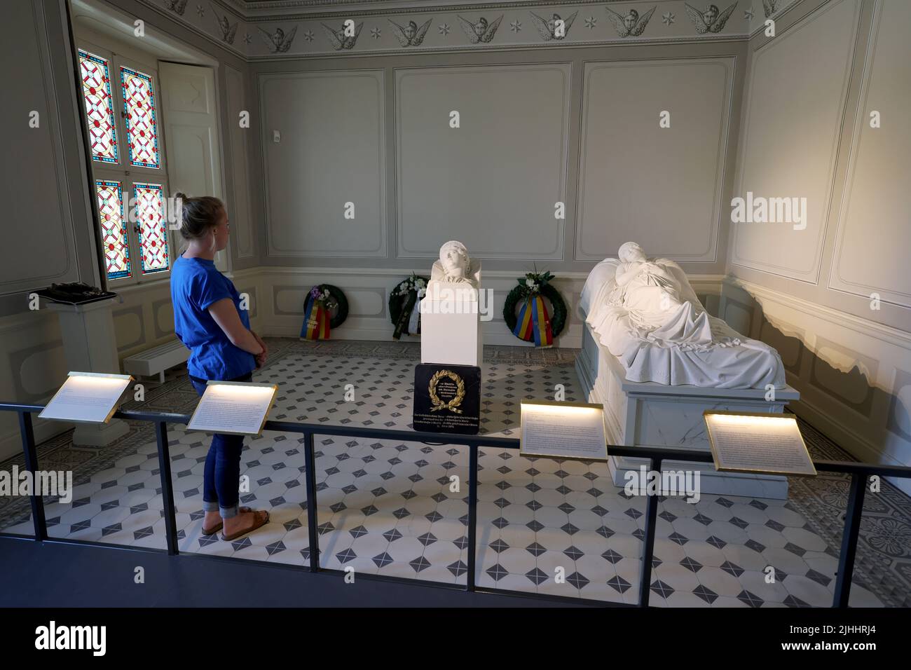 12 July 2022, Mecklenburg-Western Pomerania, Hohenzieritz: Christine Henning, Museum Education, is standing in the death chamber of Queen Luise of Prussia (1776 -1810) in the palace next to the 'Bust Segment of the Tomb Figure of Queen Luise' (c. 1820 - 1830) by Christian Daniel Rauch. On the right lies the 'Grave Figure of Queen Luise of Prussia' (plaster cast of the Neustrelitz marble copy). The original bust has now been returned to the memorial. The bust is to be presented in Hohenzieritz on 'Luise Day' (19.07.2022) on the occasion of the 212th anniversary of the death of the once beloved Stock Photo