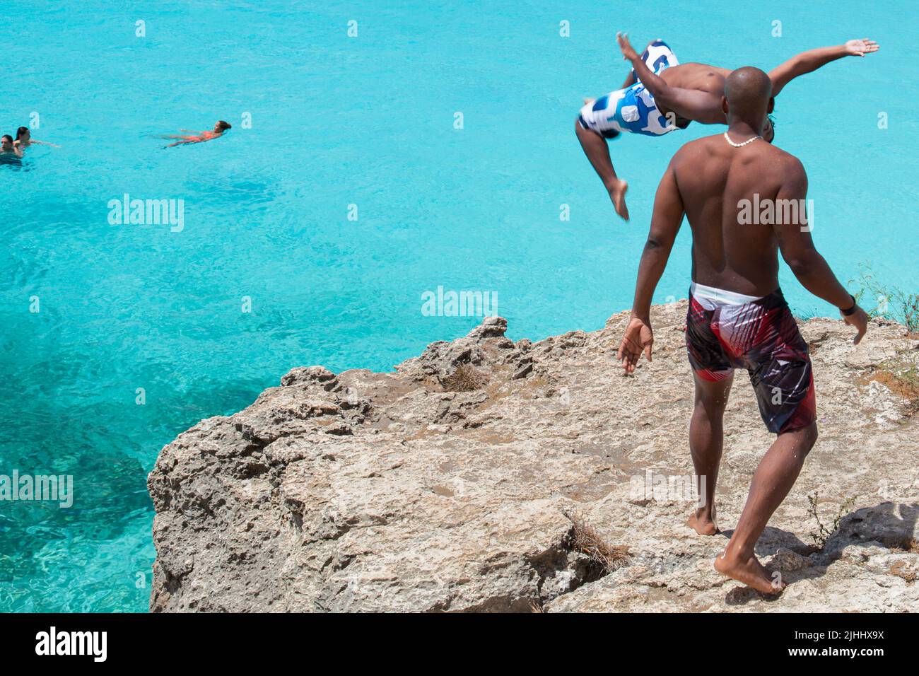 young man jumping off cliff into water. Stock Photo