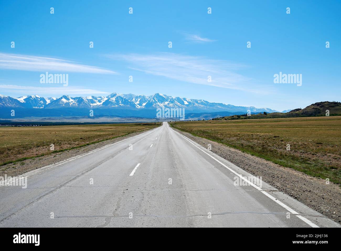 A straight road goes into the distance into a snowy mountain range ...