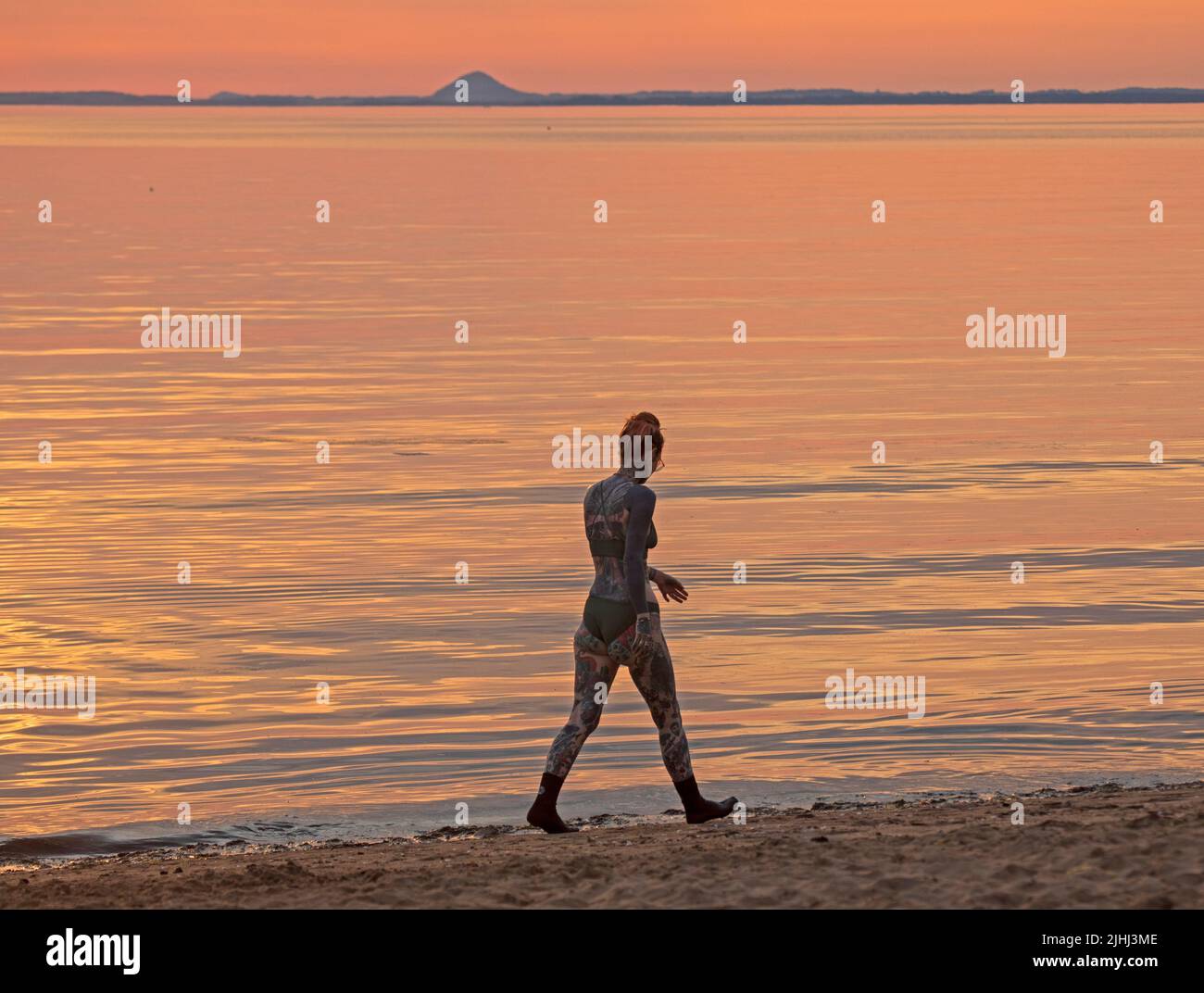 Portobello, Edinburgh, Scotland,UK. 19thJuly 2022. Subtle Sunrise at the seaside, what is predicted to be the hottest day of the year so far, temperature was 18 degrees at 6.30am for those out on the Firth of Forth. Pictured:  female walks along the shore. Stock Photo