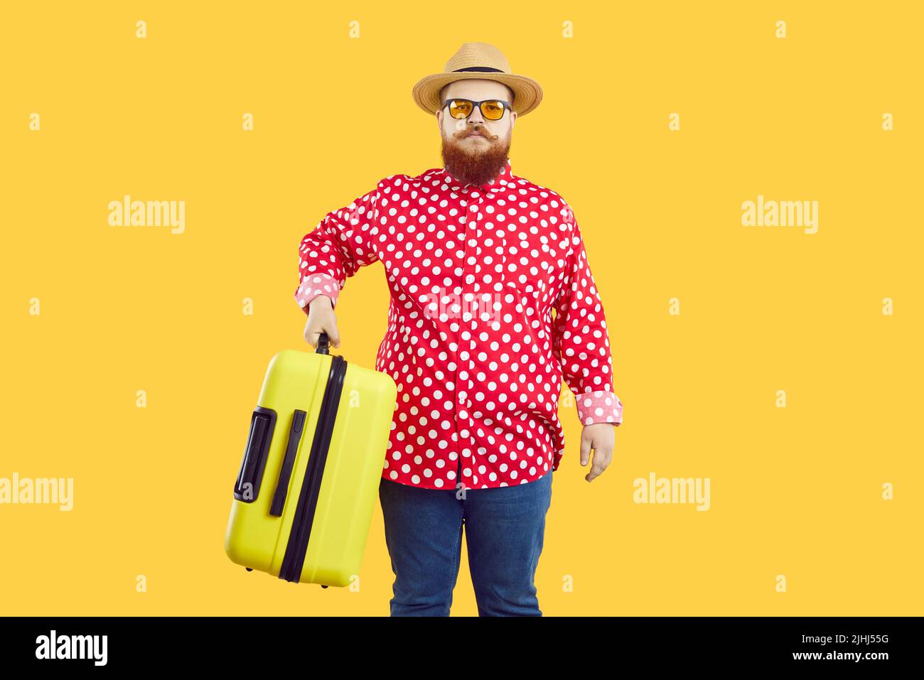 Stylish chubby man with serious expression holding heavy suitcase on orange background. Stock Photo