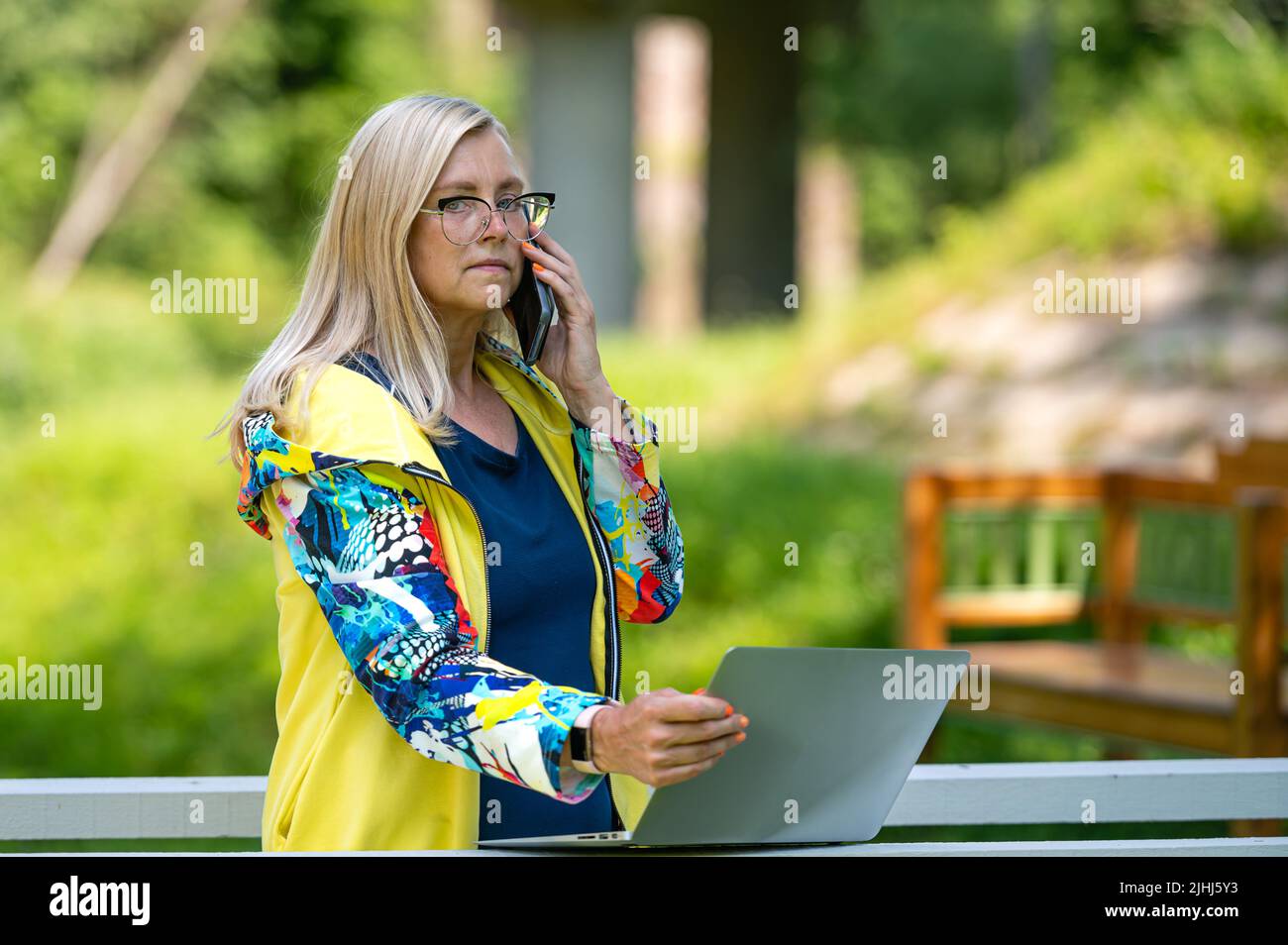 senior woman at the garden working from home using laptop and speaking ...