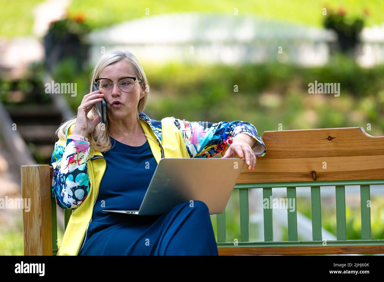 senior woman at the garden working from home using laptop and speaking ...