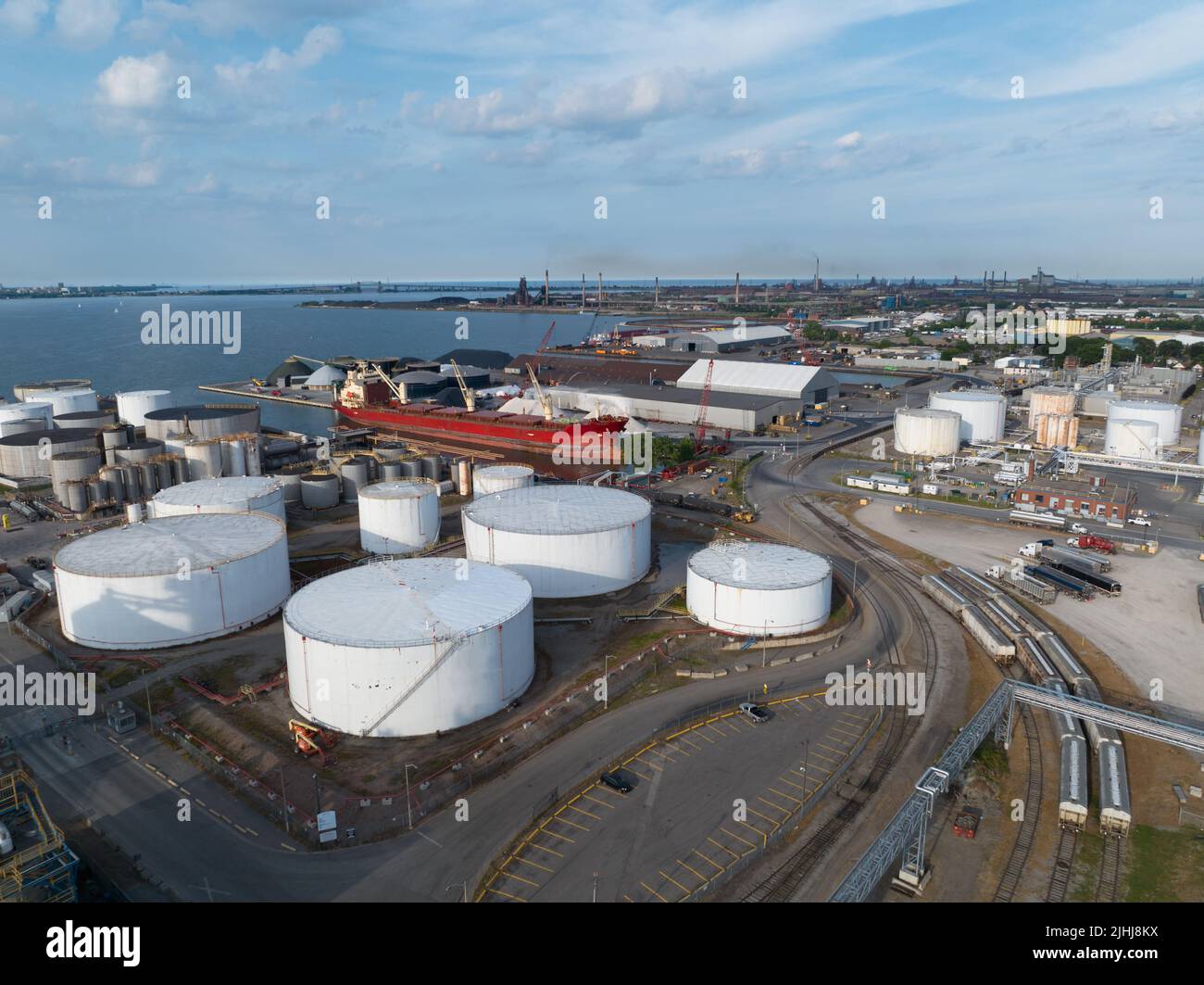 An aerial view of a white petroleum or oil tank field located next to a port. Pictured during the day while a cargo vessel is stationary. Stock Photo