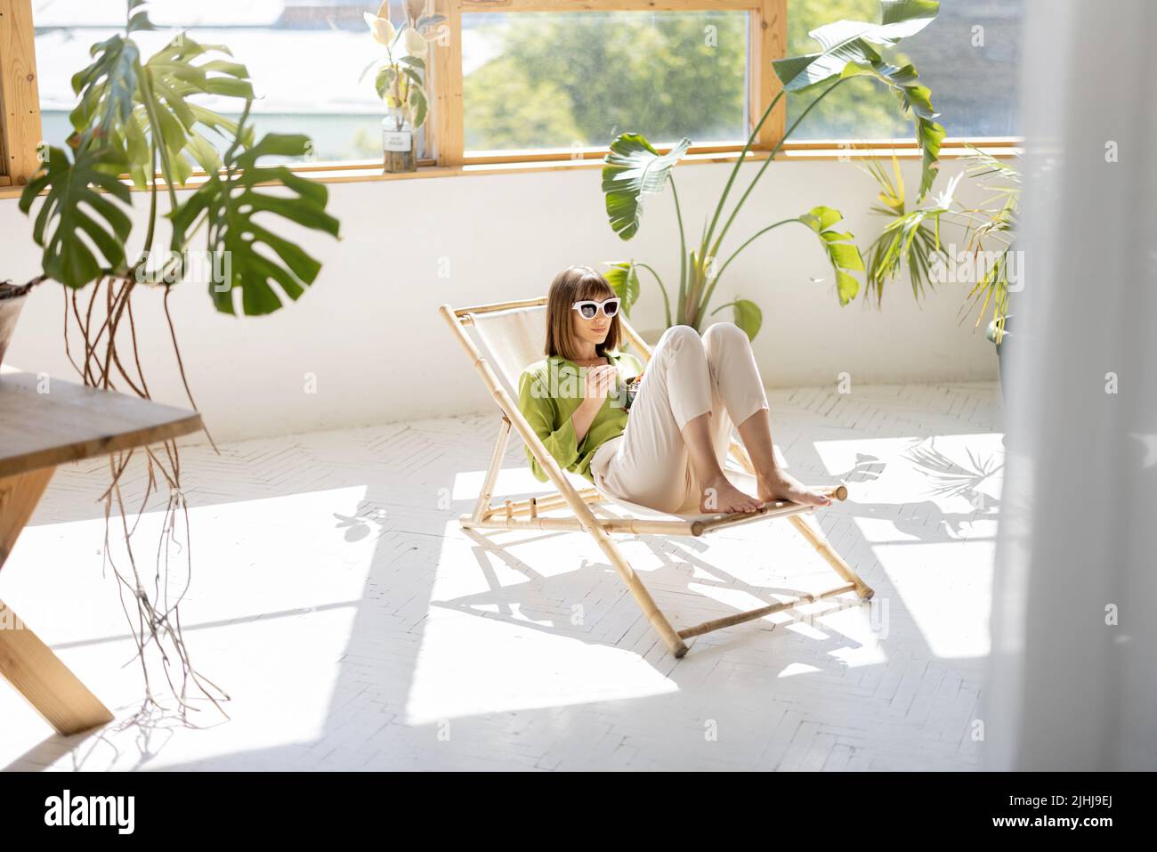 Woman sits relaxed with a drink in room with plants Stock Photo