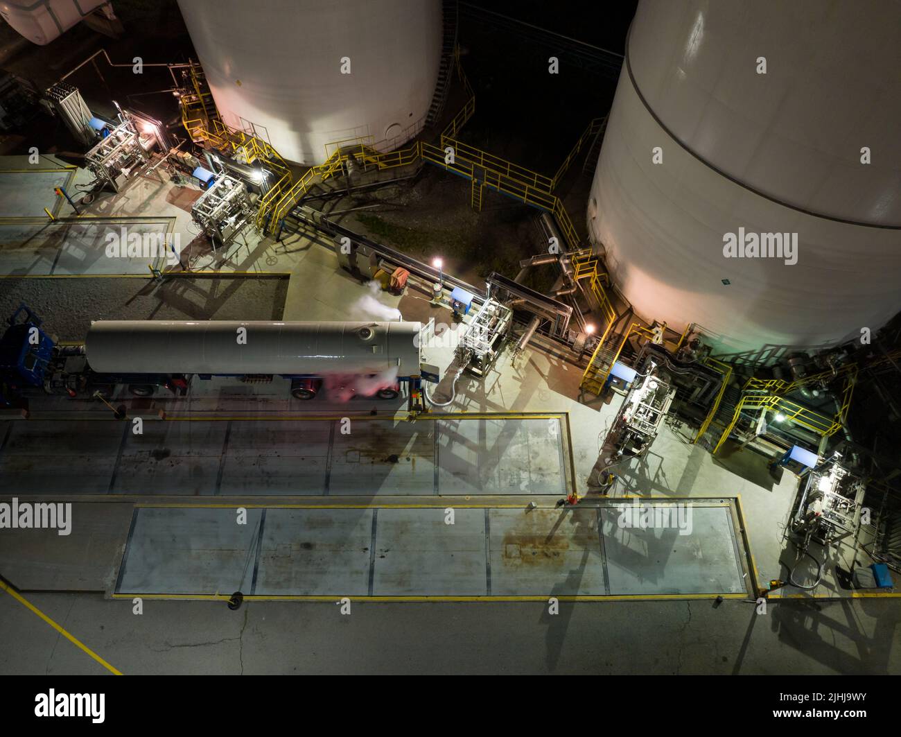 An aerial view above a large liquid gas facility as a transport tanker is being filled late at night, under bright lights. Stock Photo