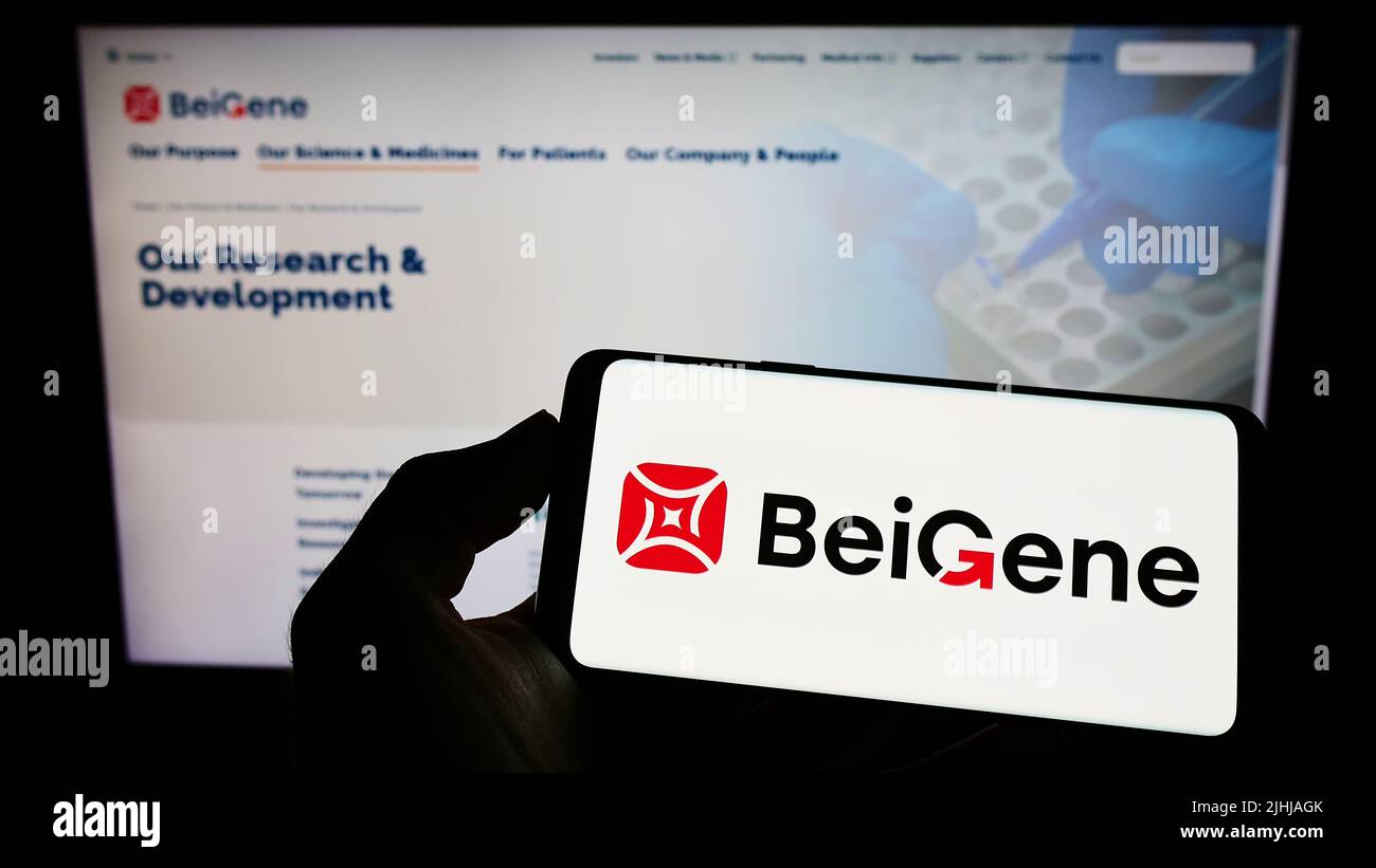 Person holding mobile phone with logo of Chinese biotechnology company Beigene Ltd. on screen in front of web page. Focus on phone display. Stock Photo