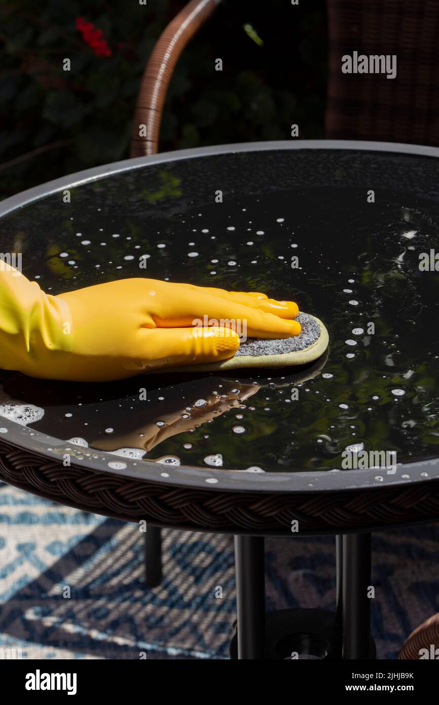 Person wearing rubber gloves cleaning a glass top patio table in a