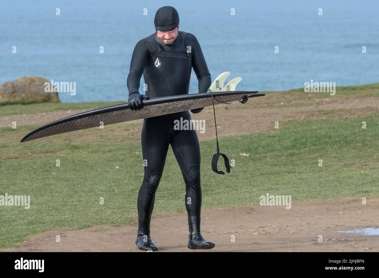 A surfer examining his surfboard after surfing at Fistral in Newquay in