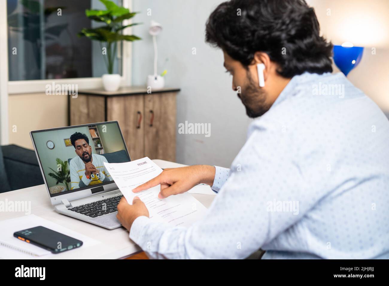 Recruiter busy taking online or virtual interview of applicant by seeing resume at office - concept of job, employment or consultation. Stock Photo