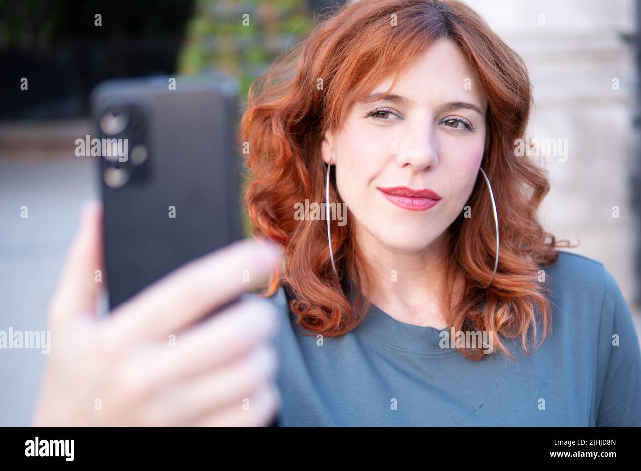 portrait of ginger woman outdoors with cellphone front camera making a