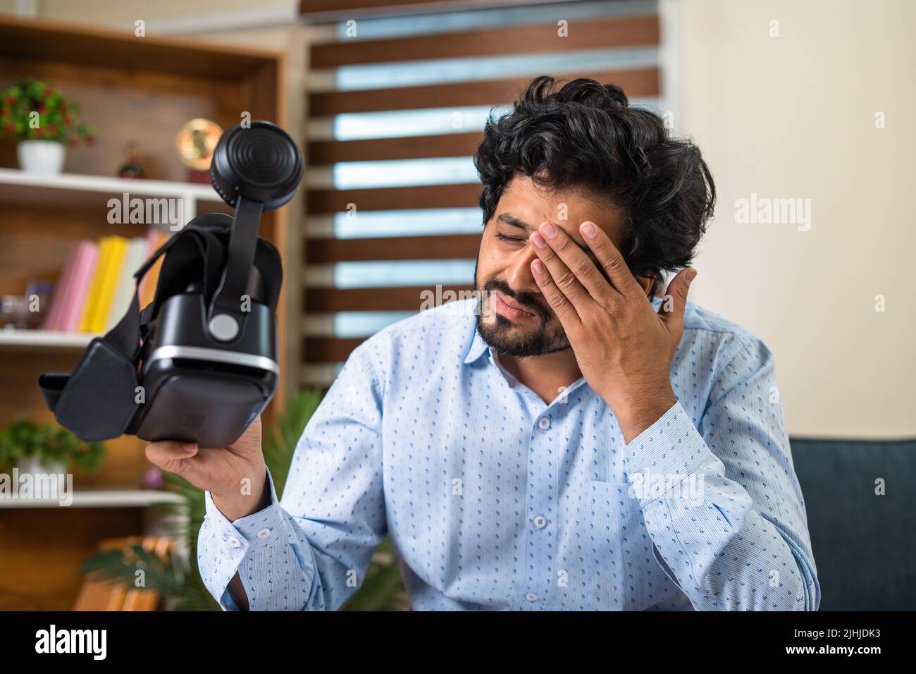 young man rubbing his eyes after extensive use of VR or virtual reality goggles at office for meeting - concept of technology, metaverse and virtual Stock Photo