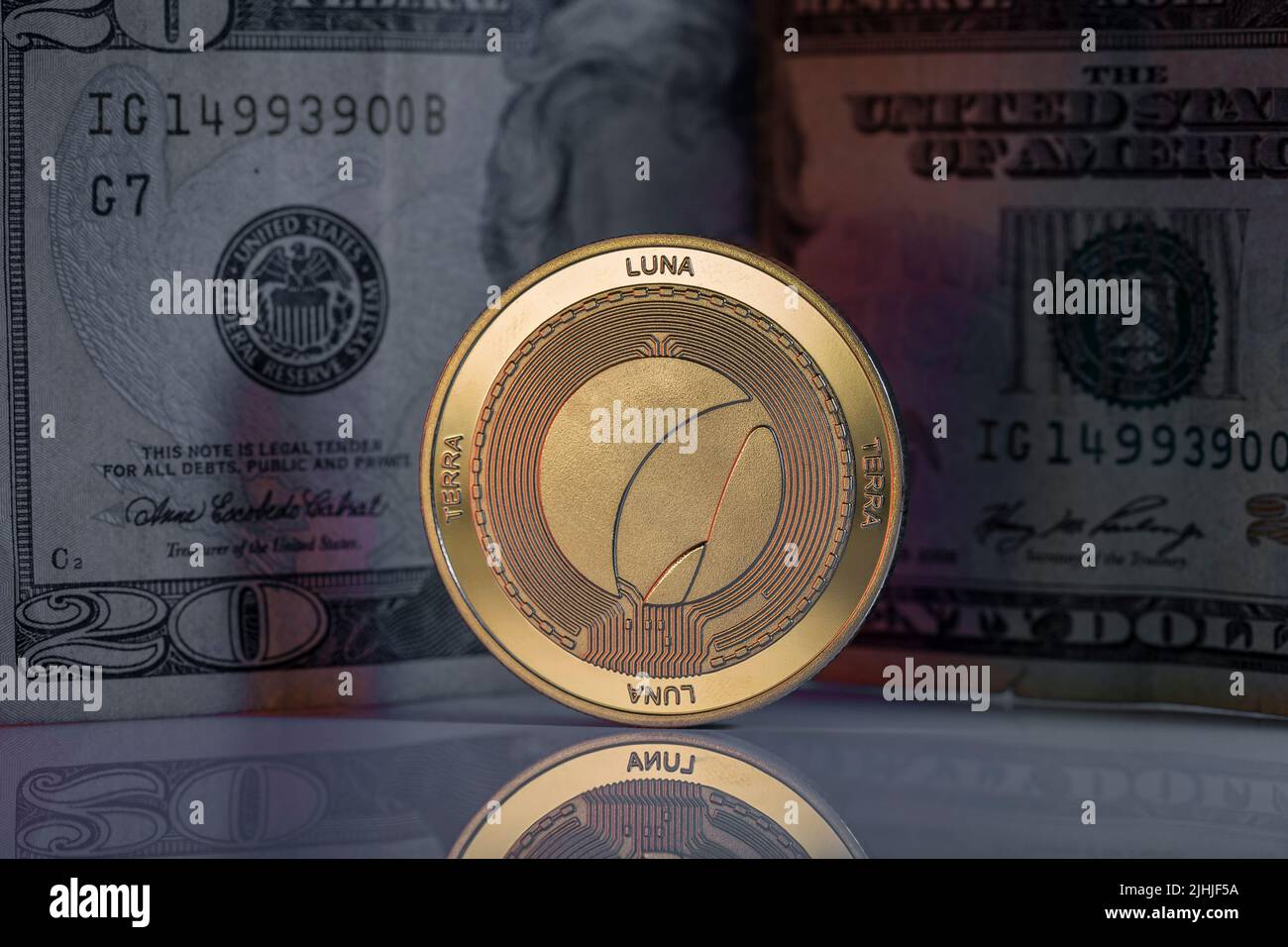 Terra Luna LUNC Cryptocurrency Physical Coin Placed on reflective surface with twenty dollar bill behind. Stock Photo