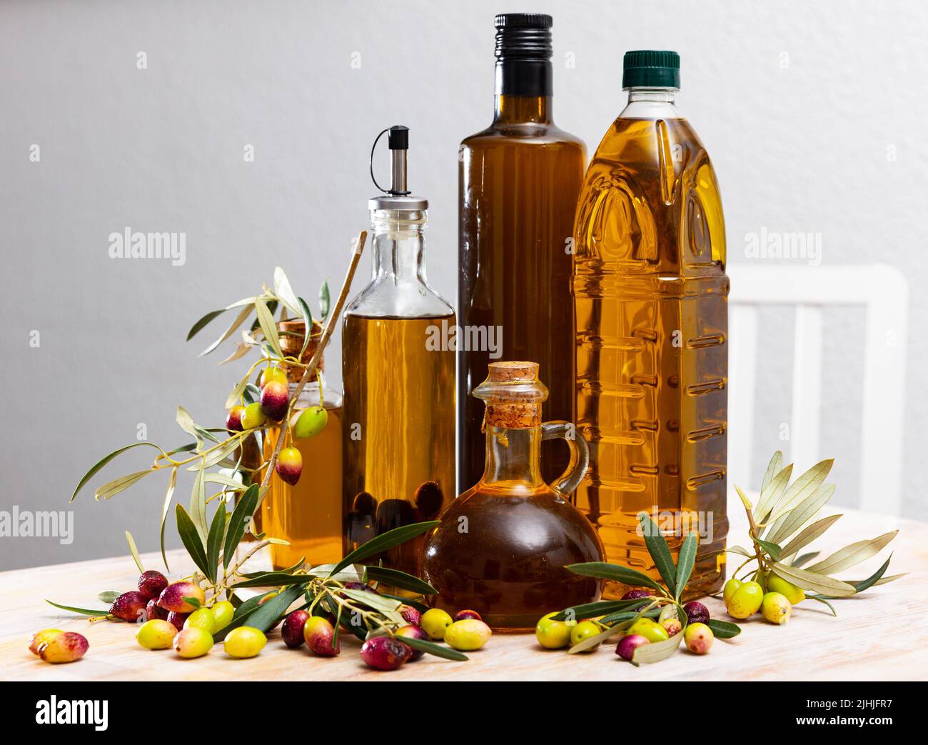 Glass bottles and carafes with fresh olive oil on wooden table with olive branches and fresh