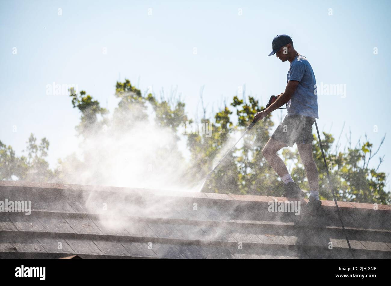 Rustington, West Sussex, UK. Tuesday 19th July 2022. A man uses a jet wash to clean a house roof this morning as the heat continues to incease, near the south coast. Credit: Geoff Smith/Alamy Live News Stock Photo