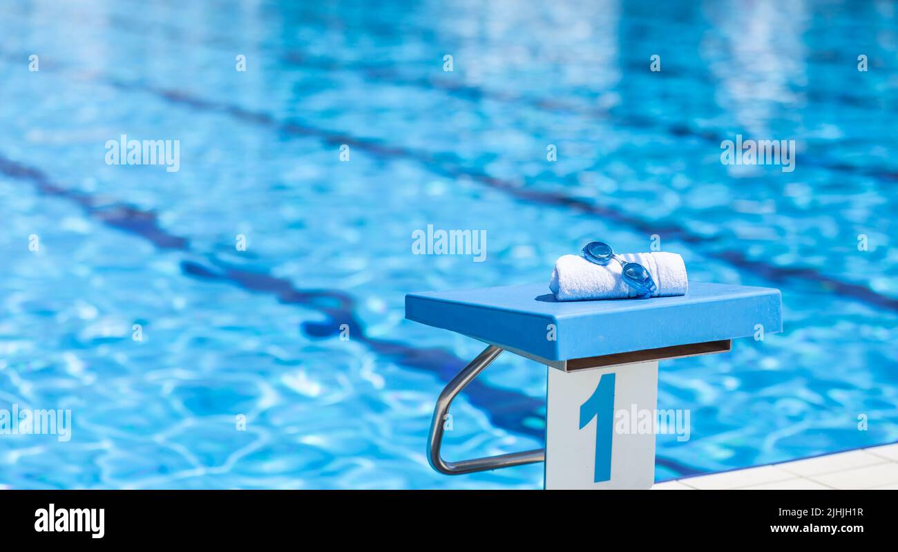 Swimming goggles and a towel placed on the starting bridge by the swimming pool. Stock Photo