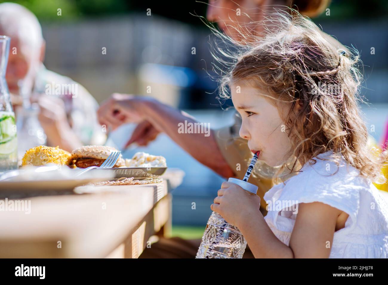 Family eating at barbecue party dinner in garden, little girl drinking water and enjoying it. Stock Photo