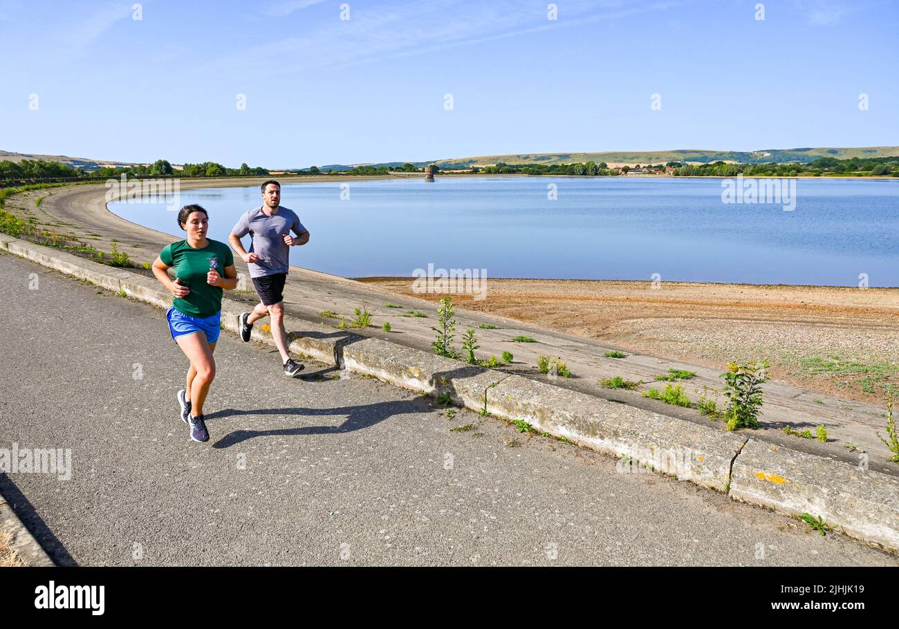 Lewes UK 19th July 2022 - Early morning runners at Arlington Reservoir near Lewes in East Sussex on another hot sunny day with temperatures forecast to exceed 40 degrees in some parts as an extreme red weather warning has been issued for today throughout parts of Britain : Credit Simon Dack / Alamy Live News Stock Photo
