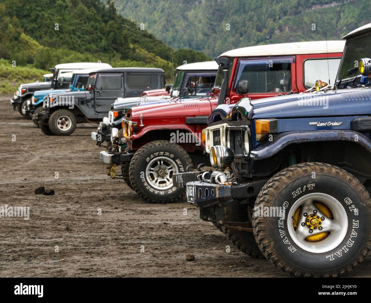 Classic Japanese jeep parking in line for tourist transport at Mount Bromo in the Tengger Semeru National Park with green hill in background. Stock Photo