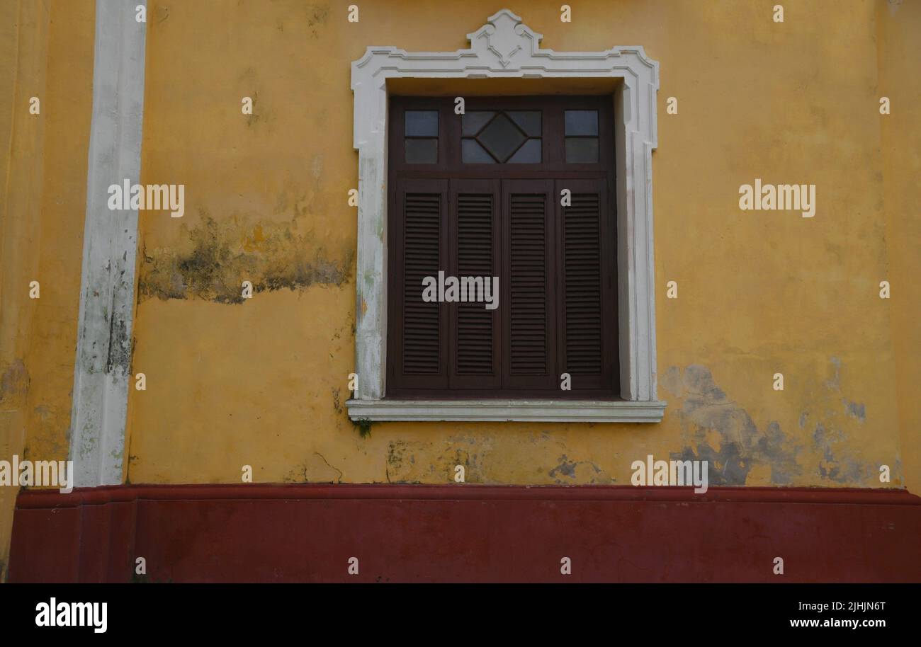 Antique window with brown wooden shutters on a weathered ochre stucco