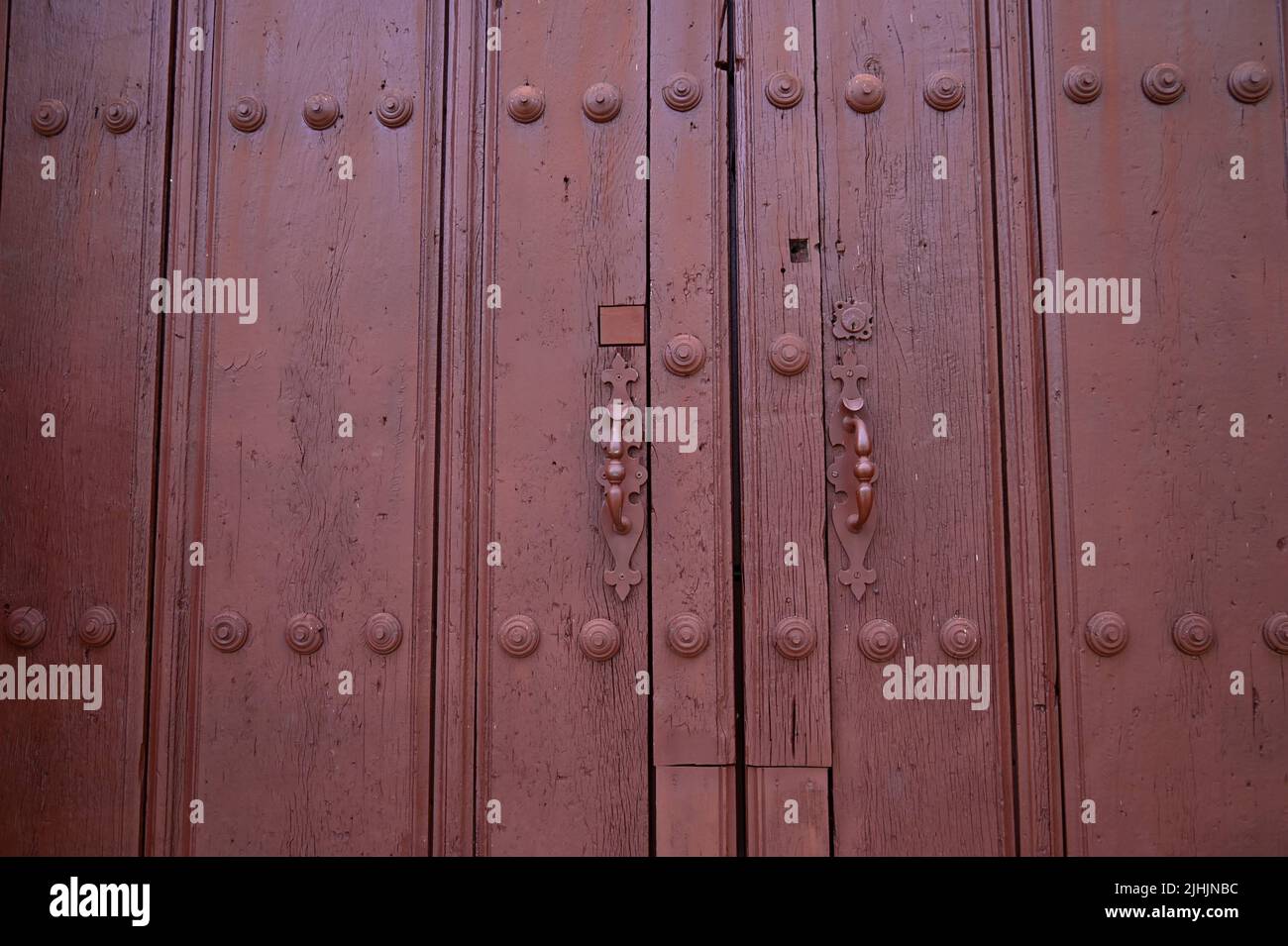 Antique red wooden door with matching studs and iron handles in