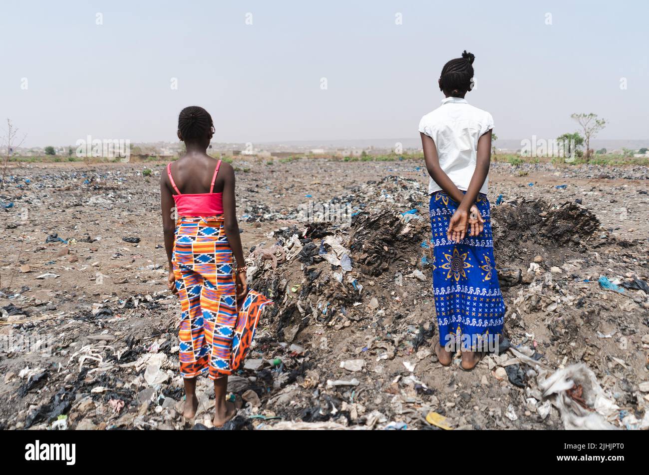 Two teenage girls standing in a landfill, symbolizing the lack of future prospects for young Africans struggling with pollution, global warming and a Stock Photo