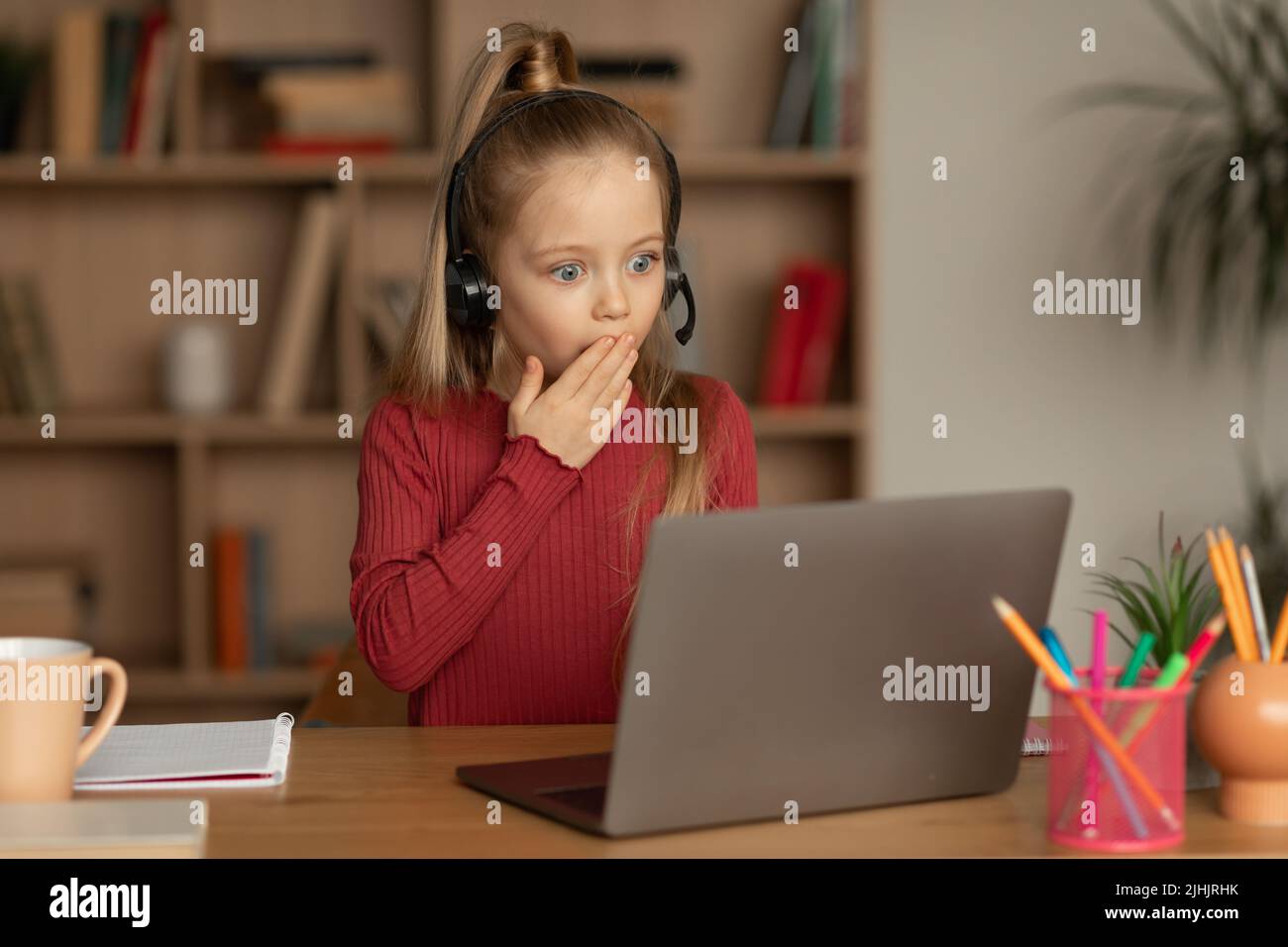 Shocked Kid Girl Looking At Laptop Computer Learning Online Indoors Stock Photo