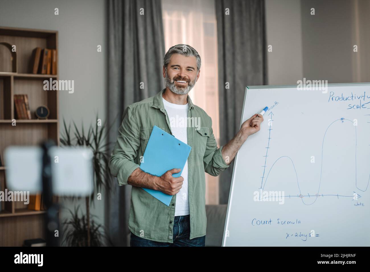 Cheerful aged european male teacher with beard has meeting with students, pointing at blackboard Stock Photo