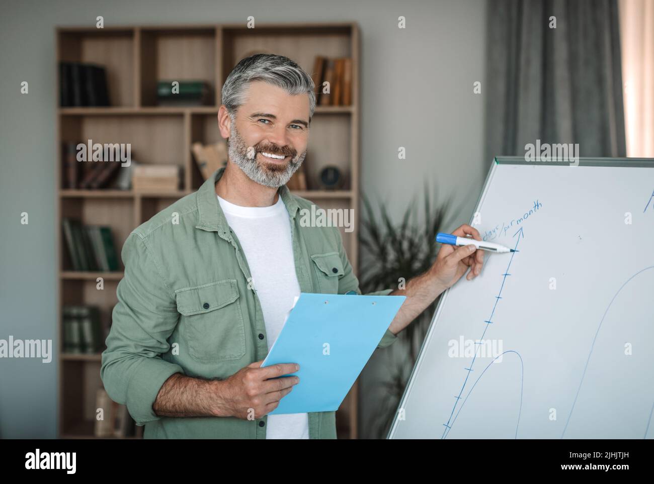Glad mature european male teacher with beard has meeting with students, write on blackboard in room Stock Photo